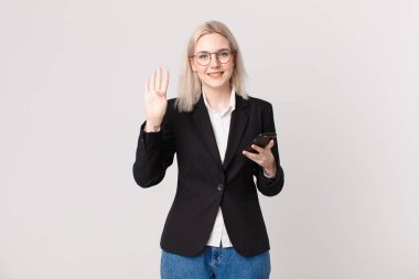 Sarışın, güzel bir kadın gülümsüyor ve arkadaş canlısı görünüyor, dört numarayı gösteriyor ve elinde bir cep telefonu var.