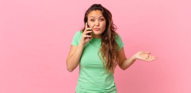 Genç, güzel bir kadın şaşkın, şaşkın, şüpheci ve akıllı bir telefon tutuyor.