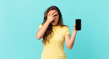 Genç, güzel bir kadın şok olmuş, korkmuş ya da korkmuş görünüyor. Yüzü elle kaplanmış ve elinde akıllı bir telefon tutuyor.