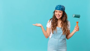 Genç, güzel bir kadın neşeyle gülümsüyor, mutlu hissediyor ve bir konsept gösteriyor ve bir duvar boyuyor.