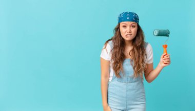 Genç, güzel bir kadın kafası karışmış ve bir duvar boyuyor.