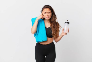 Genç ve güzel bir kadın kafası karışık ve şaşkın hissediyor, deli olduğunu gösteriyor. fitness konsepti
