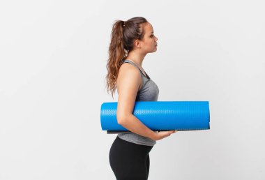 Profilde güzel bir kadın hayal ediyor, hayal ediyor ya da hayal ediyor ve yoga minderi tutuyor.