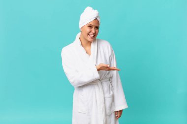 Genç, güzel bir kadın neşeyle gülümsüyor, mutlu hissediyor ve bir konsept gösteriyor ve duştan sonra banyo bornozu giyiyor.