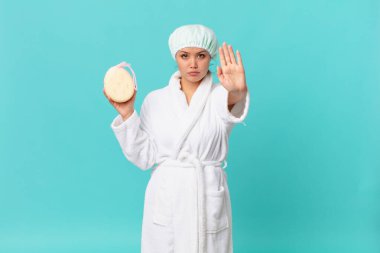 Genç ve güzel bir kadın ciddi görünüyor. Avuç içi gösteriyor, jest yapıyor ve duştan sonra banyo cübbesi giyiyor.