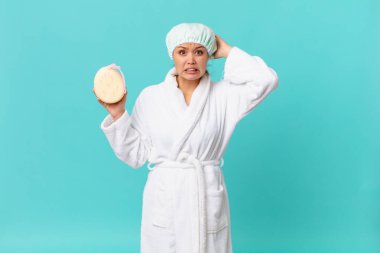 Genç, güzel bir kadın kendini stresli, endişeli ya da korkmuş hissediyor. Elleri başının üstünde ve duştan sonra banyo bornozu giyiyor.