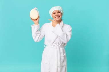 Genç, güzel bir kadın neşeyle gülümsüyor, mutlu hissediyor ve yan tarafı gösteriyor ve duştan sonra banyo cübbesi giyiyor.