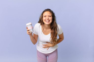 Genç ve güzel bir kadın kahkahalarla kahkahalarla gülüyor ve elinde kahve tutuyor.