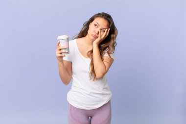 Genç ve güzel bir kadın yorgun ve uykulu bir şekilde sıkılmış hissediyor ve elinde kahve tutuyor.
