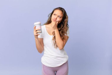 Genç, güzel bir kadın düşünüyor, kuşkulu ve kafası karışık hissediyor ve elinde bir kahve tutuyor.