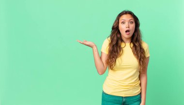 Genç ve güzel bir kadın şaşırmış ve şok olmuş görünüyor. Çenesi düşmüş, elinde bir nesne tutuyor ve kopyalama alanını işaret ediyor.