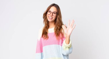 Genç, güzel bir kadın, mutlu bir şekilde gülümsüyor, el sallıyor, sizi selamlıyor.