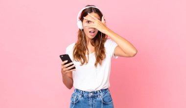 Genç, güzel bir kadın şok olmuş, korkmuş ya da korkmuş görünüyor. Kulaklıkla ve akıllı telefonla yüzünü kapatıyor.