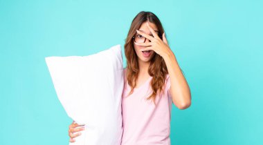 Genç, güzel bir kadın şok olmuş, korkmuş ya da korkmuş görünüyor. Yüzü pijamayla kaplı ve elinde yastıkla.