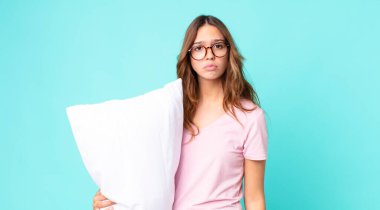 Genç ve güzel bir kadın üzgün ve mızmız görünüyor. Mutsuz görünüyor ve ağlıyor. Pijama giyiyor ve yastık tutuyor.
