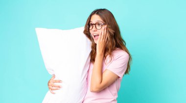Genç, güzel bir kadın mutlu, heyecanlı ve şaşırmış pijama giyiyor ve yastık tutuyor.