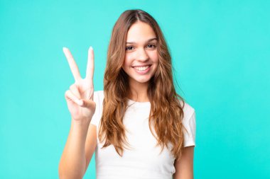 Gülümseyen ve mutlu görünen genç güzel bir kadın zafer ya da barış işareti yapıyor.