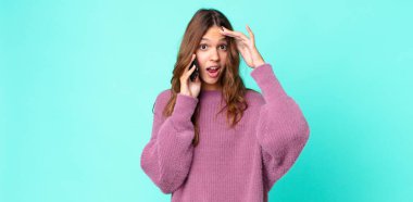 Genç ve güzel bir kadın mutlu görünüyor, şaşırmış ve şaşırmış ve akıllı telefon kullanıyor.