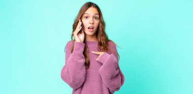 Genç ve güzel bir kadın ağzı açık, kendini gösteren ve akıllı telefon kullanan şok olmuş ve şaşırmış görünüyor.