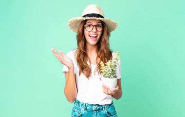 Genç, güzel bir kadın kendini mutlu ve şaşkın hissediyor. Hasır şapkası ve kaktüsüyle inanılmaz bir şey.