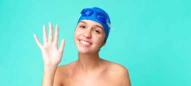 Genç, güzel bir kadın mutlu bir şekilde gülümsüyor, el sallıyor, sizi yüzme gözlükleriyle selamlıyor.