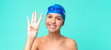 Genç, güzel bir bayan gülümsüyor ve arkadaş canlısı görünüyor. Yüzme gözlükleriyle dört numarayı gösteriyor.