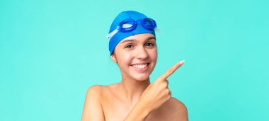 Genç, güzel bir kadın neşeyle gülümsüyor, mutlu hissediyor ve yüzme gözlükleriyle bir tarafı işaret ediyor.