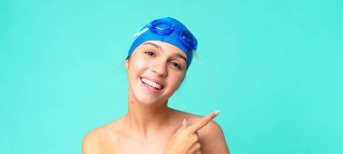 Genç ve güzel bir kadın heyecanlı ve şaşırmış görünüyor. Yüzme gözlükleriyle yan tarafı işaret ediyor.