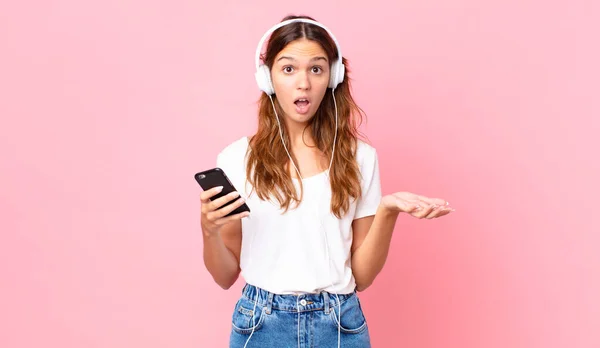 Młoda Ładna Kobieta Zdumiona Zszokowana Zdumiona Niesamowitą Niespodzianką Słuchawkami Smartfonem — Zdjęcie stockowe