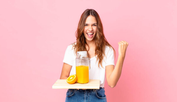 young pretty woman shouting aggressively with an angry expression and holding a tray with an orange juice