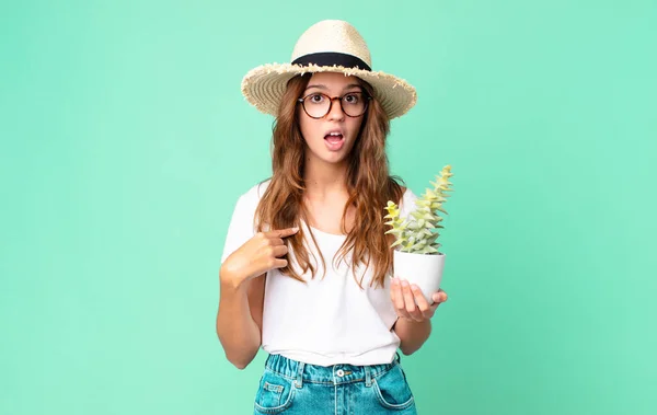 年轻漂亮的女人满嘴惊讶地看着自己 用草帽指着自己 拿着仙人掌 — 图库照片