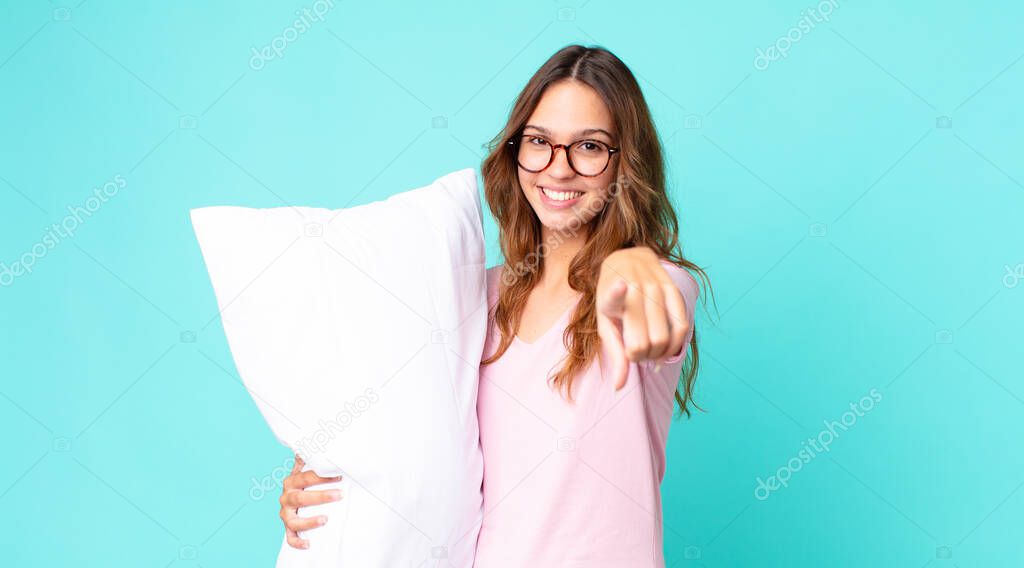 young pretty woman pointing at camera choosing you wearing pajamas and holding a pillow