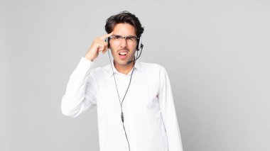 Genç İspanyol adam şaşkın ve şaşkın hissediyor, senin deli olduğunu gösteriyor. tele pazarlamacı konsepti