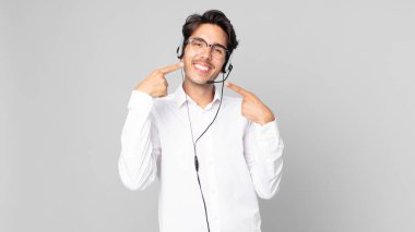 Genç İspanyol adam kendine güvenerek gülümsüyor ve kendi gülüşünü gösteriyor. tele pazarlamacı konsepti