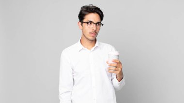 Genç İspanyol bir adam üzgün, üzgün ya da kızgın hissediyor ve yan tarafa bakıyor ve elinde kahve tutuyor.