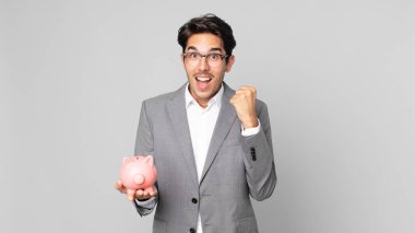 Genç İspanyol adam şokta, gülüyor, başarıyı kutluyor ve kumbarasını elinde tutuyor.