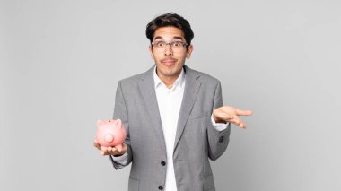 Genç İspanyol adam şaşkın, şaşkın, kuşkucu ve kumbarayı elinde tutan