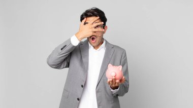 Genç İspanyol bir adam şok olmuş, korkmuş ya da korkmuş görünüyor. Yüzü elle kaplanmış ve elinde domuz kumbarası var.