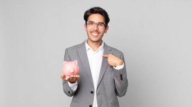 Genç İspanyol bir adam mutlu hissediyor ve heyecanlı bir kumbarayla kendini işaret ediyor.