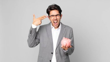 Genç İspanyol adam mutsuz ve stresli görünüyor, intihar jesti silah işareti yapıyor ve elinde domuz kumbarası var.