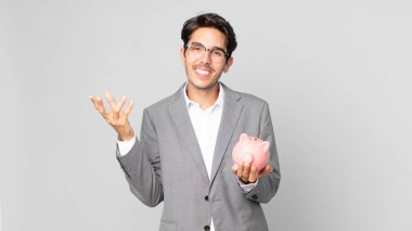 Genç İspanyol adam mutlu, şaşırmış bir şekilde çözümü ya da fikri fark ediyor ve elinde bir kumbara tutuyor.