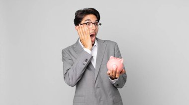 Genç İspanyol adam mutlu, heyecanlı ve şaşırmış hissediyor ve elinde bir kumbara tutuyor.