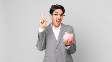 Genç İspanyol bir adam, bir fikri fark edip elinde bir kumbara tutarak mutlu ve heyecanlı bir dahi gibi hissediyor.