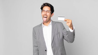 Neşeli ve asi tavırları olan genç İspanyol bir adam şaka yapıyor, dilini dışarı çıkarıyor ve elinde bir kredi kartı tutuyor.