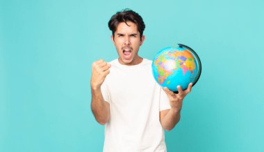 Genç İspanyol bir adam öfkeli bir ifadeyle saldırganca bağırıyor ve elinde bir dünya haritası tutuyor.