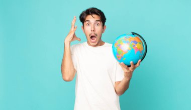 Genç İspanyol adam ellerini havaya kaldırıp bağırıyor ve elinde bir dünya haritası tutuyor.