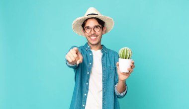 Genç İspanyol bir adam kamerayı işaret ederek seni seçiyor ve elinde bir kaktüs tutuyor.