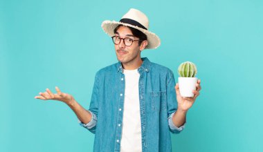 Genç İspanyol adam şaşkın, şaşkın, şüpheci ve elinde bir kaktüs tutuyor.