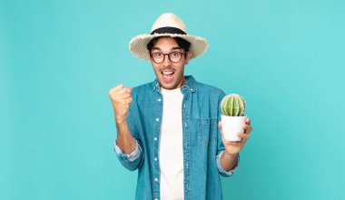 Genç İspanyol adam şok olmuş hissediyor, gülüyor ve başarıyı kutluyor ve elinde bir kaktüs tutuyor.