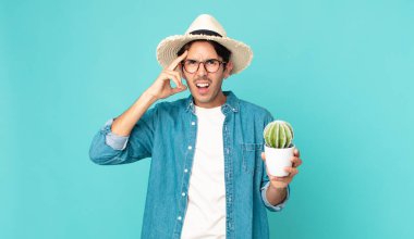 Genç İspanyol adam mutlu, şaşkın, şaşırmış ve elinde bir kaktüs tutuyor.